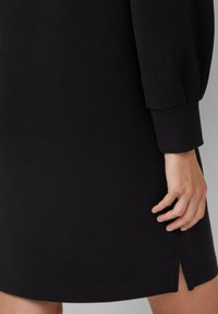 Schwarzes Strickkleid mit langen Ärmeln, geradem Schnitt und seitlichem Schlitz, aus weichem Baumwoll-Mix.