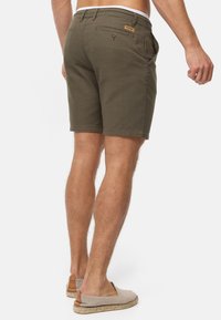 Shorts vert olive au design ajusté avec un tissu texturé. L'arrière présente une petite poche avec un bouton et une étiquette de marque.