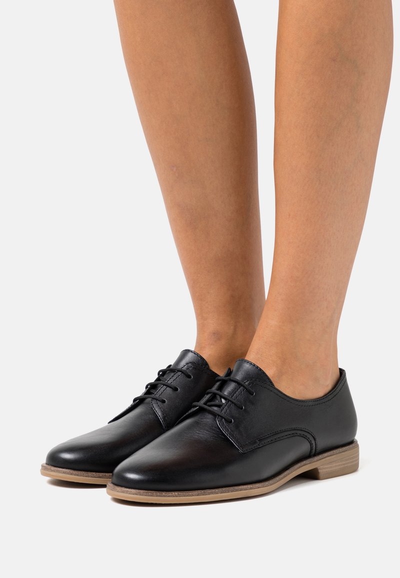 Chaussures habillées en cuir noir à texture lisse, bout arrondi et design à lacets. Présentent une semelle extérieure marron clair pour le contraste.