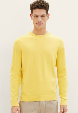 Suéter de punto amarillo con cuello redondo, mangas largas y puños acanalados. La tela parece suave con una textura sutil.