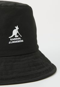 Fekete vödörkalap texturált felülettel, az elején fehér kenguru logóval és a "KANGOL J.LINDEBERG" felirattal.
