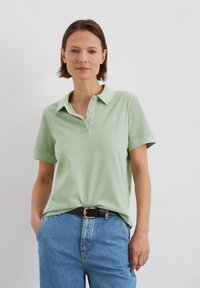 Lichtgroen polo T-shirt met een kraag en drie knopen, gecombineerd met hooggelegen blauwe spijkerbroek en een zwarte riem.