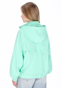 Chaqueta cortavientos de verde menta claro con capucha, puños elásticos y cintura ajustada. Tela lisa, resistente al agua y con detalles mínimos.