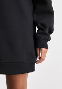Svart sweatshirtklänning med ribbad mudd, med en avslappnad passform och mjuk yta. Nederkanten är något rundad och är snyggt avslutad.