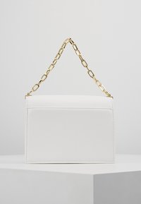 Vit läderhandväska med en strukturerad form, försedd med en guldkedjeslinga och en minimalistisk design. Slät textur utan synliga mönster.