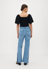 Svart topp med puffede ermer og firkantet utringning, kombinert med lyseblå vide jeans med sideslit. Modell som står med ryggen til kameraet.
