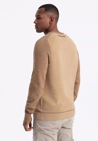 Maglione beige a pullover con texture a costine sulle spalle e sull'orlo, dotato di un corpo liscio, scollatura rotonda e una piccola etichetta con logo sul retro.