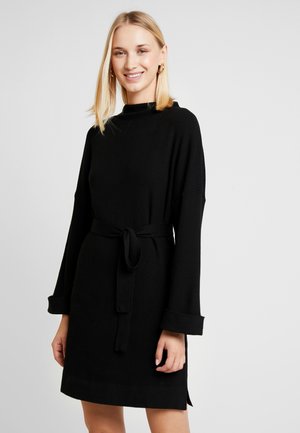 Zwarte gebreide jurk met een hoge halslijn, lange klokmouwen en een riem op de taille. Gewatteerde stof met een effen kleur en zijsplitten.