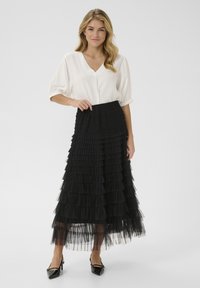 Black tiered maxi skirt made of tulle with a fitted waistband, paired with a white, short-sleeved blouse featuring a V-neckline.