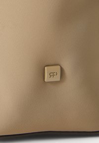 Bež torba s teksturom koja ima mali zlatni logo u donjem kutu. Površina je glatka s dijagonalnim uzorkom, što dodaje dimenziju.