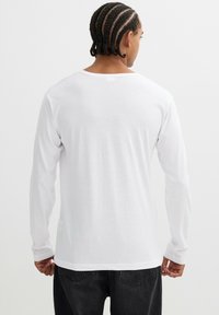 Camiseta blanca de manga larga hecha de algodón suave, con un escote redondo y un ajuste relajado, sin marcas ni diseños visibles.