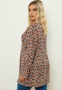 Blus med lång ärm i krämfärgad med blommönster, med multifärgade blommor i röd, brun och blå, med en vågig nederkant och avslappnad passform.