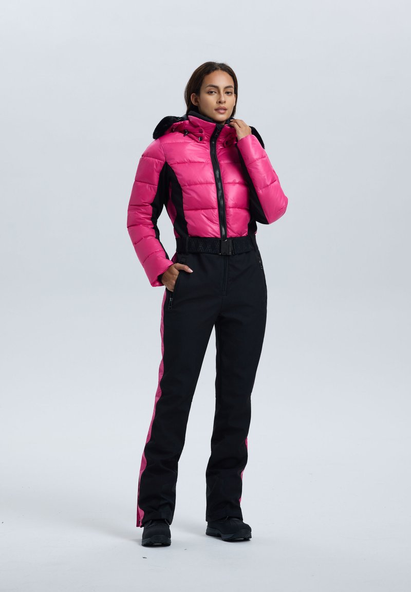 Chaqueta rosa acolchada con detalles negros, cuello alto y cremallera. Pantalones negros con franjas laterales rosas y bolsillos. Calzado negro completa el conjunto.