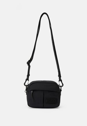 Kleine zwarte crossbodytas met verstelbare band, voorvak met rits en geperst "HUGO" logo op een effen witte achtergrond.