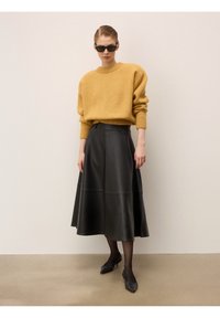 Pull en tricot oversized moutarde, jupe en cuir noir, ballerines noires et lunettes de soleil. Texture lisse, coupe décontractée et silhouette arrivant au genou.