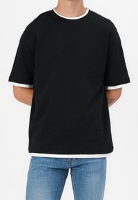 Czarny bawełniany t-shirt z okrągłym dekoltem, z białym wykończeniem przy kołnierzu i rękawach. Luźny krój z krótkimi rękawami.