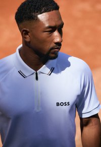 White short-sleeve polo shirt with a zip collar, featuring a textured surface and a black "BOSS" logo on the left chest.