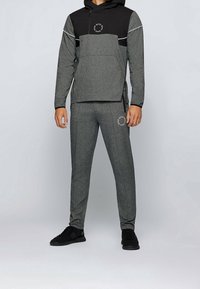 Conjunto deportivo gris que incluye una sudadera negra con capucha, cierre y logo, combinada con pantalones grises a juego, ambos en una tela texturizada.