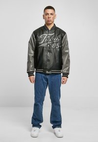 Black leather varsity jacket with gray sleeves, featuring "Jibu League 05" on the front, paired with blue jeans and white sneakers.