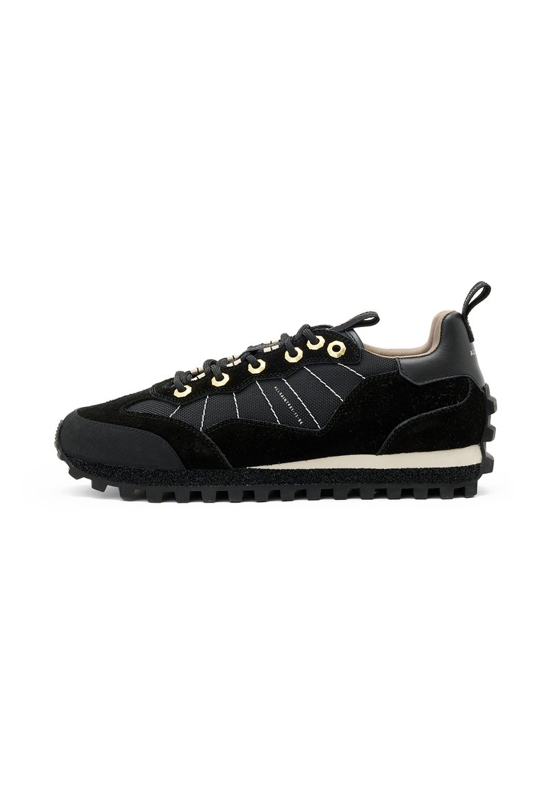Sneaker nera con un mix di materiali in suede e mesh, cuciture intricate, occhielli dorati e una suola in gomma testurizzata.
