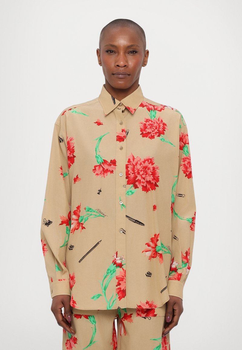 Camisa floral en beige con patrones de flores rojas y verdes, hecha de tela suave. Presenta un diseño de botonadura y mangas largas.