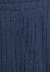 Donkerblauwe ribbelstof met verticale strepen en een zachte textuur, met een zichtbare naad en zakdetails.