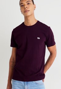 T-shirt à manches courtes, col rond, de couleur bordeaux foncé, fabriqué en coton doux, avec un petit logo "Lee" blanc sur la poitrine.
