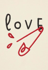 Parola "love" ricamata in nero con una spilla da balia rossa ricamata che sostituisce la lettera "v" su uno sfondo di tessuto beige.