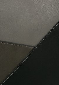 Textil de cuero con un diseño geométrico en tonos grises y negros, con texturas contrastantes y costuras finas a lo largo de los bordes.