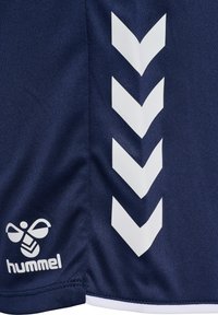 Marineblåt sportstof med hvide chevron-striber og en bi-logo, med ordet "hummel" trykt med små bogstaver.