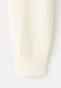 Manche de pull en tricot couleur crème avec un poignet côtelé, présentant une texture douce et des motifs fins tissés sur toute la surface.