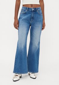 Jeans azuis rectos feitos de denim, com uma cintura alta, cinco bolsos, desbotamento suave e fecho de botão. A bainha é larga e termina no tornozelo.