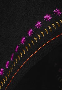 Tissu noir avec trois lignes parallèles de points brodés : des étoiles roses vives, des feuilles jaunes et des points orange unis.