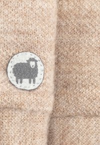 Beige Wolle mit einer weichen Textur, die einen runden grauen Fleck zeigt, auf dem ein Schaf abgebildet ist. Das Material wirkt warm und gemütlich.