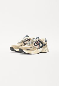 Beige en marine sneakers van mesh en suede materiaal. Voorzien van een dikke witte zool, zwarte rubberen loopzool en reflecterende accenten op de veters.
