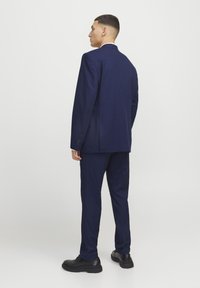 Traje azul marino con corte entallado y chaqueta de una sola abertura, combinado con pantalones a juego y zapatos de piel negra. Textura suave, diseño clásico.