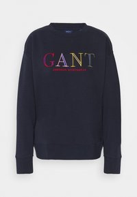 Felpa blu navy con scollo rotondo, caratterizzata da un logo "GANT" ricamato multicolore e la scritta "AMERICAN SPORTSWEAR" in rosso. Tessuto morbido.