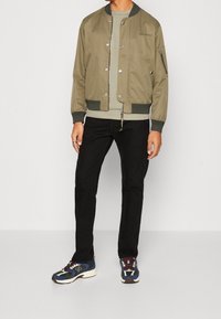 Oliivinvihreä bombariparka vetoketjulla edessä, resorilla varustetut hihansuut ja taskut, yhdistetty vaaleanvihreään paitaan, mustiin housuihin ja värikkäisiin tennareihin.