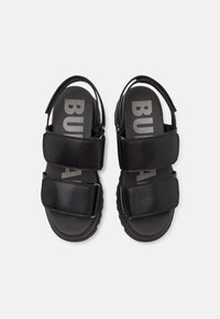 Black sandals featuring two wide straps, a textured footbed, and a thick rubber sole. Brand name printed in gray on insoles.