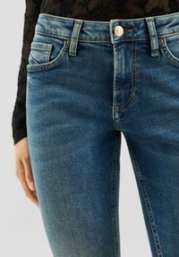 Jasnoniebieskie dżinsy z denimu mają dopasowany krój, pięć kieszeni i zapięcie na guzik. Tkanina ma gładką fakturę z delikatnym wyblaknięciem.