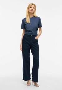 Camiseta de algodón azul marino de manga corta combinada con pantalones de pierna ancha azul marino de cintura alta. La modelo lleva sandalias plateadas de tiras.