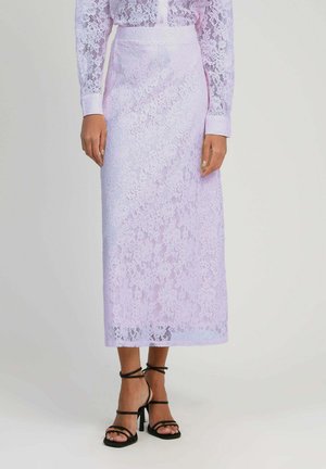 Femme portant un chemisier en dentelle lavande à manches longues, rentré dans une jupe midi en dentelle assortie, avec des sandales noires à talons hauts et à brides.