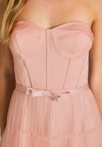 Röda rosa utan ärmar klänning med en figurnära bodice, vertikala sömdetaljer och en utsvängd tullekjol. Har en knuten rosett vid midjan.
