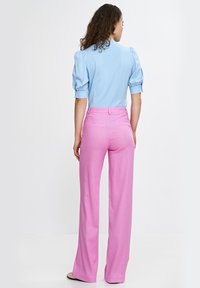 Jasnoniebieska bluzka z bufkami, zestawiona z różowymi spodniami o wysokim stanem i szerokich nogawkach, które mają gładką teksturę i subtelny połysk. Bez widocznych wzorów.
