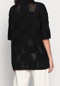 Pull noir en maille avec un motif à carreaux aux textures variées, col à revers et manches courtes.
