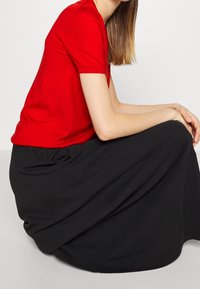 Camicetta rossa a maniche corte in tessuto liscio, abbinata a una gonna nera fluida con texture drappeggiata e una vestibilità ampia.
