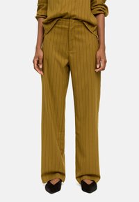 Oliwkowe spodnie z wysokim stanem w pionowe paski, o luźnym kroju i miękkiej fakturze, zestawione z czarnymi szpilkami.