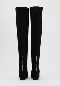 Botas negras por encima de la rodilla hechas de suave ante. Tacones cuadrados, cremalleras traseras y textura suave con una silueta elegante.