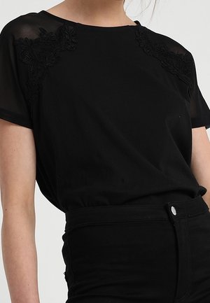 Black short-sleeve top with sheer shoulder panels and floral embroidery accents, featuring a round neckline and relaxed fit, paired with black pants.