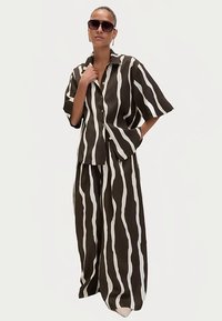 Conjunto a rayas marrón y blanco que incluye una camisa de manga corta abotonada y pantalones de pierna ancha, confeccionado con tela ligera.